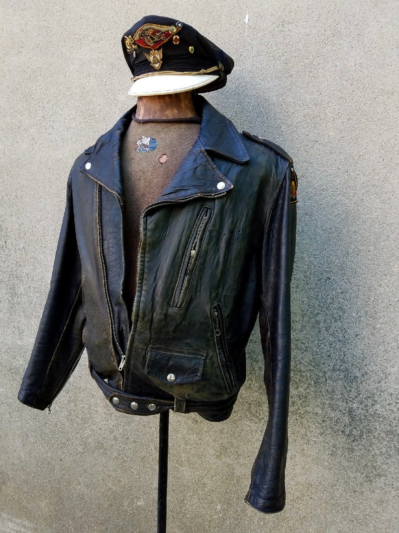 May include: A black leather biker jacket with a zip fastening and a belt. The jacket has a distressed look and features a patch on the left sleeve.