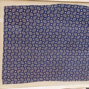 May include: A framed piece of fabric with a repeating pattern of small, light blue and gold leaves on a dark blue background.