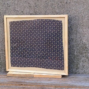 May include: A wooden frame with a black and white patterned fabric inside. The frame is standing on a wooden surface.