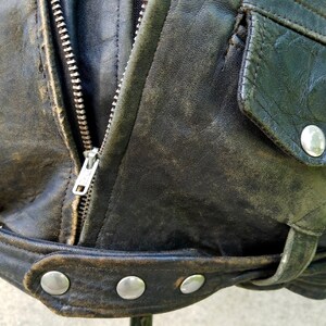 May include: A black leather jacket with a zip fastening and a flap pocket. The jacket has a worn and distressed look, with visible stitching and a belt.