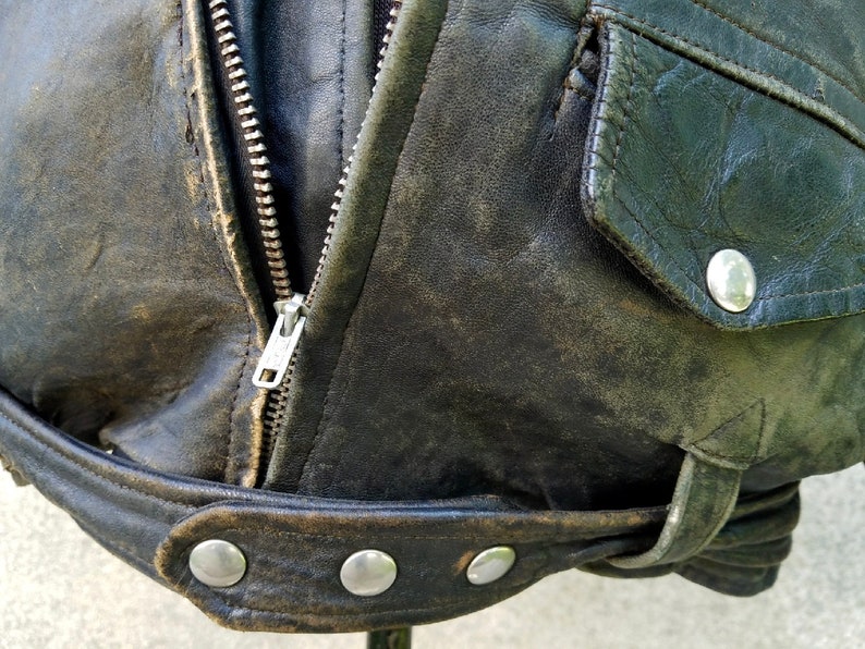 May include: A black leather jacket with a zip fastening and a flap pocket. The jacket has a worn and distressed look, with visible stitching and a belt.