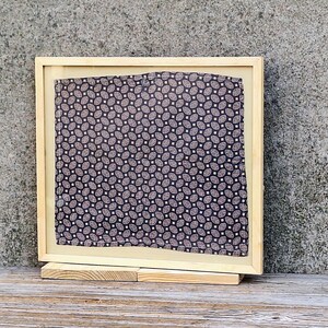 May include: A wooden picture frame with a black and white patterned fabric inside. The frame is standing on a wooden surface.
