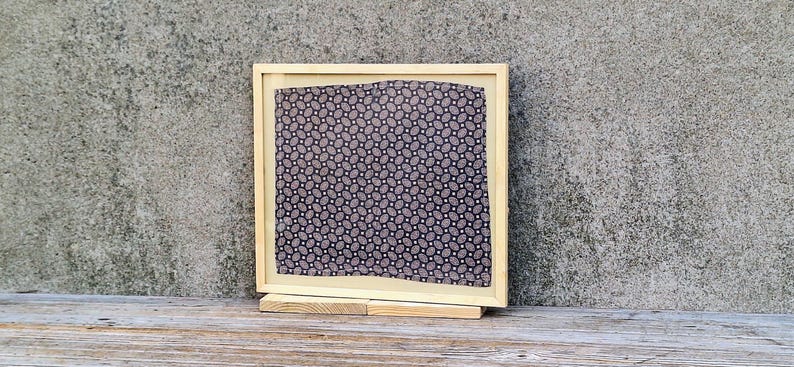 May include: A wooden picture frame with a black and white patterned fabric inside. The frame is standing on a wooden surface.