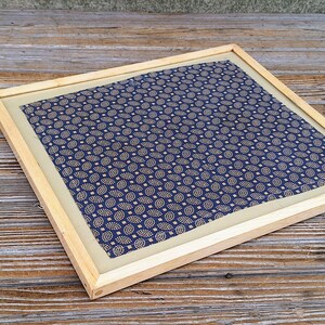 May include: A framed piece of fabric with a blue and white paisley pattern. The frame is made of natural wood.