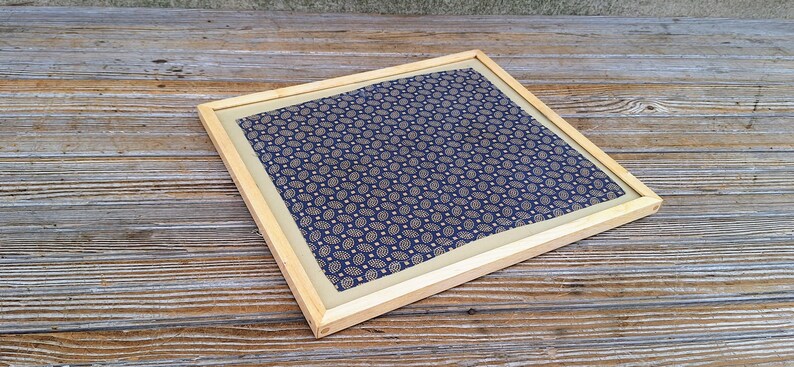 May include: A framed piece of fabric with a blue and white paisley pattern. The frame is made of natural wood.