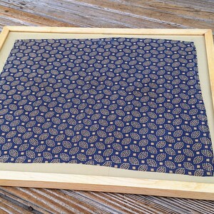 May include: A framed piece of fabric with a blue and gold pattern. The fabric has a repeating pattern of small, stylized leaves.