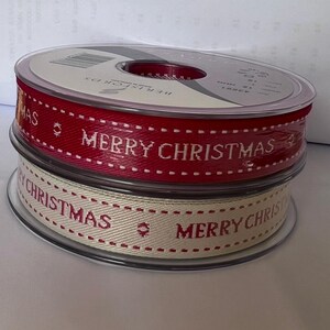 May include: Two rolls of Christmas ribbon. One roll is red with white lettering that says "Merry Christmas". The other roll is cream with red lettering that says "Merry Christmas".
