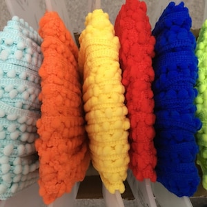 May include: Assortment of colourful pom-pom trim in pink, light blue, orange, yellow, red, blue, and neon green.