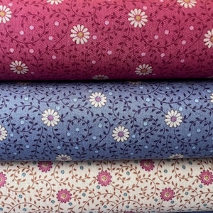 May include: Close-up of three fabric swatches with floral patterns. The top swatch is a deep pink with white daisies and small white dots. The middle swatch is blue with white daisies and blue dots. The bottom swatch is cream with pink daisies and brown vines.