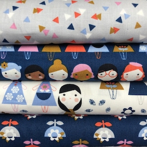 May include: Four fabric swatches with different patterns. The top swatch is light blue with white, pink, and orange triangles. The second swatch is dark blue with a repeating pattern of girls with different hair colors and outfits. The third swatch is white with a repeating pattern of girls with different hair colors and outfits. The bottom swatch is dark blue with a repeating pattern of white flowers.