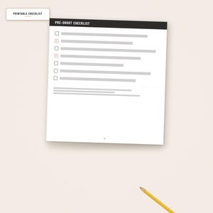 May include: A white printable checklist document with a black header labeled PRE-SHOOT CHECKLIST. It features six checkboxes, two of which are marked with checkmarks, followed by gray horizontal lines for text. A yellow pencil sits below the document.