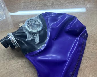 May include: A purple and black hood made of a smooth, flexible material. The hood features a black front section with a circular silver-toned eye piece covered in clear plastic, a black nozzle, and a vertical zipper along the side.