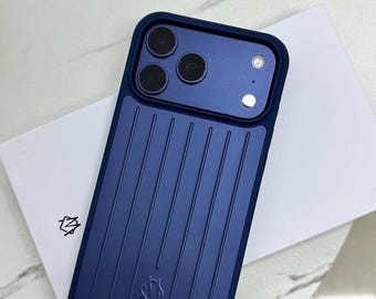 Puede incluir: Una funda para smartphone de color azul oscuro con una textura de rayas verticales en el panel posterior. La funda presenta un recorte elevado para el módulo de cámara con tres aberturas circulares y un flash. Un pequeño logotipo está grabado en la parte inferior central.