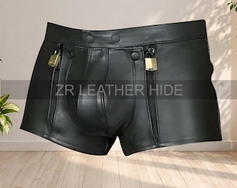 May include: Black leather shorts featuring a contoured front pouch, two vertical zippered pockets, and two small gold-tone padlocks attached to the zipper pulls. The waistband includes two snap buttons. The text ZR LEATHER HIDE is visible.