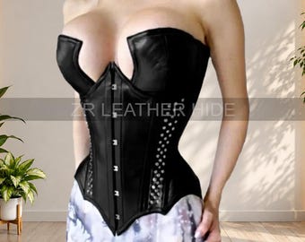 May include: A black leather corset featuring a deep, U-shaped neckline, a front hook-and-eye closure, and vertical rows of silver-toned metal studs along the side panels. The garment is structured with visible seams and a pointed hemline at the waist.