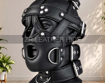 May include: A black leather head mask featuring multiple adjustable straps, silver-toned metal buckles, rivets, and D-rings. The mask includes an open mouth design and is displayed on a mannequin head. The text ZR LEATHER HIDE is visible.