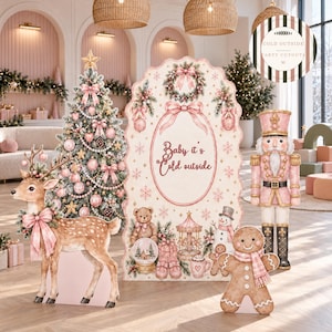 May include: A decorative Christmas party display set featuring a large arched backdrop with the text Baby it's Cold outside, a standing reindeer cutout, a nutcracker figure, and a gingerbread person, all decorated in soft pink and cream tones.