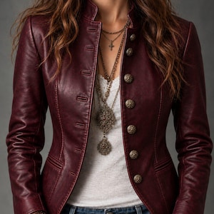 May include: A deep burgundy leather jacket featuring a high mandarin collar, long sleeves, and a front closure with ornate, round, metallic buttons. The jacket is worn over a white lace-trimmed top and blue denim jeans, accessorized with layered necklaces.