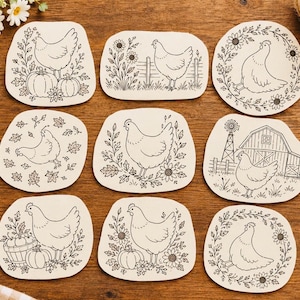 Puede incluir: Nueve posavasos de color blanco roto con formas irregulares que presentan ilustraciones de líneas negras de gallinas. Los diseños incluyen gallinas con calabazas, girasoles, un granero, un molino de viento y hojas de otoño en cada pieza.