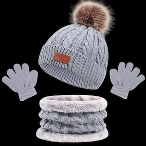 Könnte beinhalten: Ein graues Strick-Winterset bestehend aus einer Mütze mit braunem Kunstfell-Bommel und einem braunen Lederimitat-Aufnäher mit der Aufschrift FAS JEANS, passenden grauen Strickhandschuhen und einem grauen Zopfstrick-Schlauchschal mit Plüschfutter.