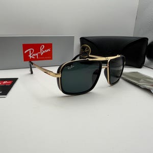 Può includere: Occhiali da sole Ray-Ban con montatura in metallo dorato, dettagli neri e lenti verde scuro. Il set include una scatola grigia marchiata, una custodia in similpelle nera, un piccolo cartellino informativo e un panno per la pulizia in plastica.