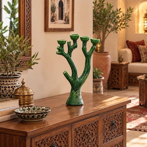 May include: A glossy, deep green ceramic candelabra shaped like a stylized tree branch with four distinct candle holders at the top. The surface has a textured, organic appearance with a vibrant, reflective glaze finish and a wide, stable base.