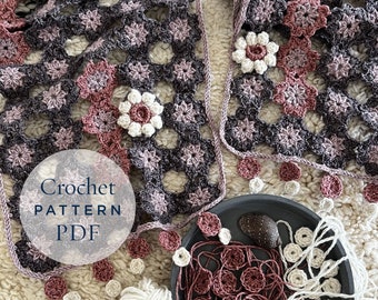 Può includere: Un modello di uncinetto PDF per una coperta con un design floreale in tonalità rosa, bianco e grigio. La coperta è realizzata con un punto a quadrato della nonna e ha un bordo a frangia.