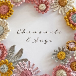 May include: A wreath of crocheted flowers in shades of pink, yellow, and gray. The flowers are arranged in a circle around the text "Chamomile & Sage".