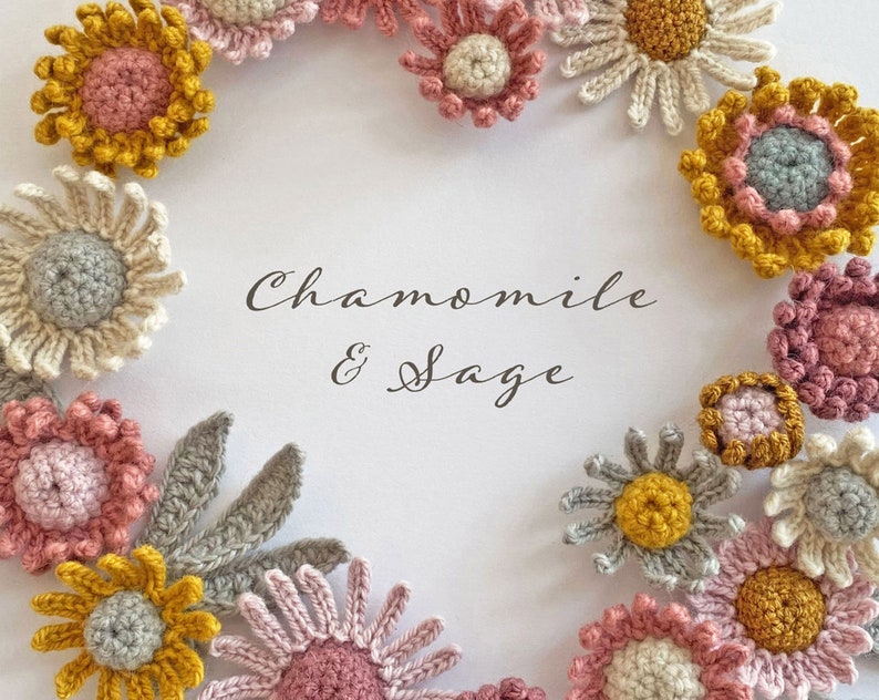 May include: A wreath of crocheted flowers in shades of pink, yellow, and gray. The flowers are arranged in a circle around the text "Chamomile & Sage".