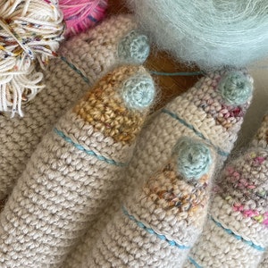 K&ouml;nnte beinhalten: F&uuml;nf geh&auml;kelte Fingerpuppen mit verschiedenen farbigen Akzenten. Die Puppen sind aus beigefarbenem Garn gefertigt und haben blaue und wei&szlig;e Akzente.
