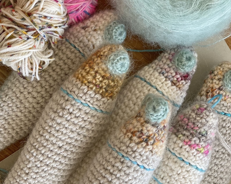 K&ouml;nnte beinhalten: F&uuml;nf geh&auml;kelte Fingerpuppen mit verschiedenen farbigen Akzenten. Die Puppen sind aus beigefarbenem Garn gefertigt und haben blaue und wei&szlig;e Akzente.