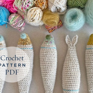 Peut inclure: Patron de crochet PDF pour réaliser cinq poissons amigurumi. Les poissons sont crochetés en fil blanc avec des accents bleus et jaunes. Les poissons sont disposés en rangée sur une surface grise. Le texte "Crochet Pattern PDF" est écrit en blanc sur un cercle blanc.