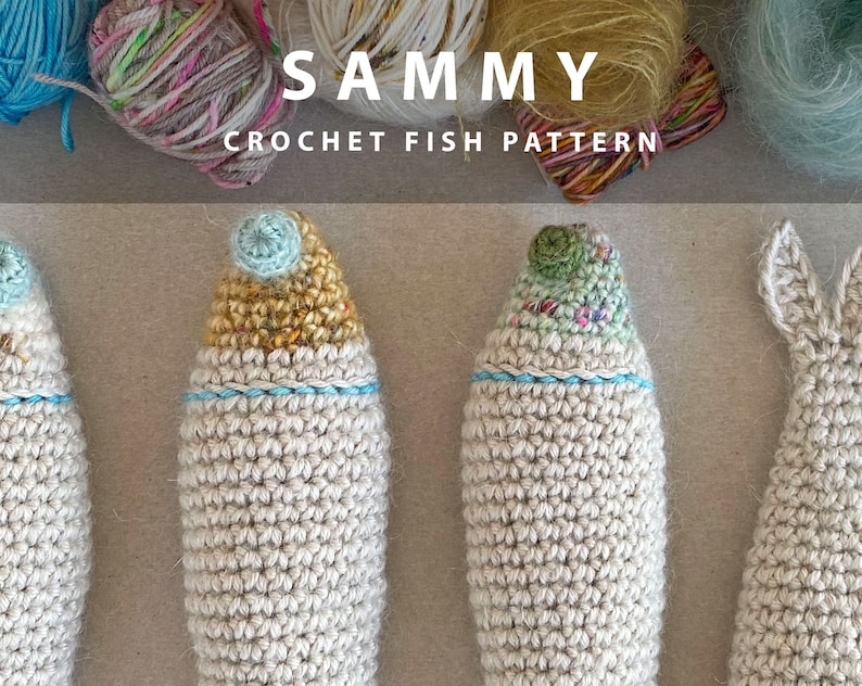 K&ouml;nnte beinhalten: Vier geh&auml;kelte Fisch-Amigurumi-Spielzeuge in verschiedenen Farben. Die Fische sind aus wei&szlig;em Garn gefertigt und haben unterschiedlich farbige Details an ihren K&ouml;pfen. Die Fische sind in einer Reihe auf einer braunen Oberfl&auml;che angeordnet. Der Text "SAMMY CROCHET FISH PATTERN" ist &uuml;ber den Fischen angezeigt.