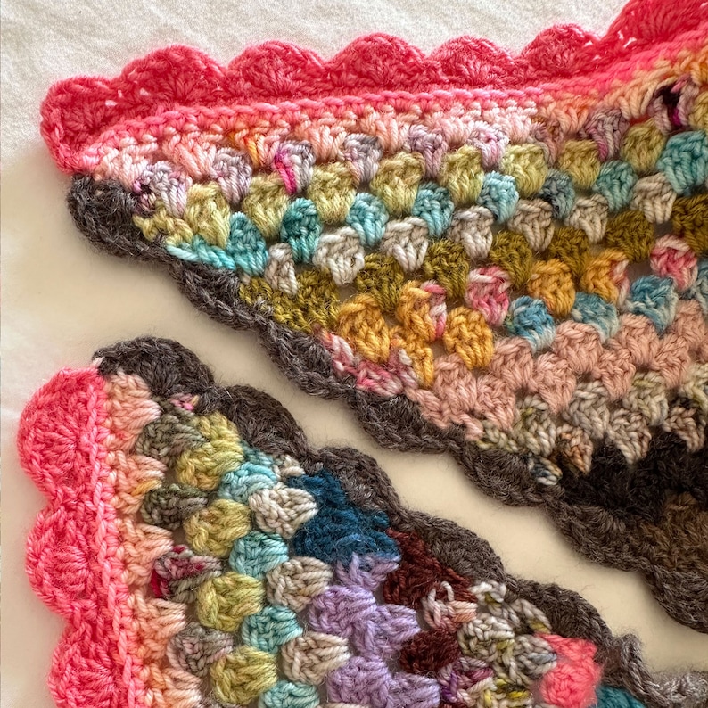 May include: A colorful crocheted shawl with a scalloped edge. The shawl is made with a variety of colors, including pink, blue, green, and yellow.