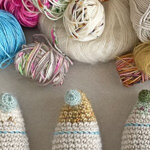 K&ouml;nnte beinhalten: Drei geh&auml;kelte Gnom-Ornamente mit verschiedenen farbigen H&uuml;ten. Der Gnom links hat einen hellblauen Hut, der Gnom in der Mitte einen gelben Hut und der Gnom rechts einen gr&uuml;nen Hut.