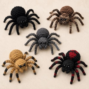 Puede incluir: Cinco juguetes de araña tejidos a ganchillo dispuestos en grupo. Una es negra sólida, una marrón, una gris oscuro, una color canela con puntas de patas marrón oscuro y una negra con detalles rojos en las patas y un patrón de corazón rojo.