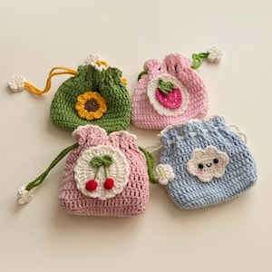 May include: Four small, handmade crochet drawstring pouches in various colours. One green pouch features a yellow sunflower, a pink one has a strawberry, another pink one displays two red cherries, and a light blue pouch shows a white smiling cloud.