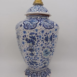 Puede incluir: Un tarro de jengibre de cerámica con base blanca y complejos patrones florales azules que cubren toda la superficie. El tarro cuenta con una tapa a juego rematada con un pequeño remate azul y dorado. El cuerpo tiene una forma hexagonal.