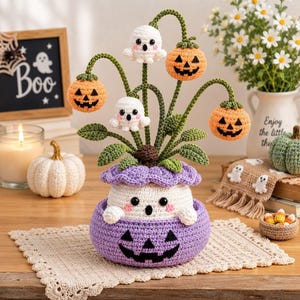 May include: A crocheted Halloween decoration featuring a purple jack-o'-lantern base containing a white ghost. Green stems emerge from the top, supporting two white ghosts and three orange jack-o'-lanterns, all accented with green leaves.