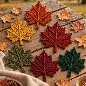 Könnte beinhalten: Ein Set aus sechs gehäkelten Ahornblatt-Untersetzern in herbstlichen Farben wie Orange, Gelb, Rot, Olivgrün und Dunkelgrün, angeordnet auf einer Holzoberfläche zusammen mit getrockneten Blättern, einem Tannenzapfen und einer kleinen Schale mit Honig.