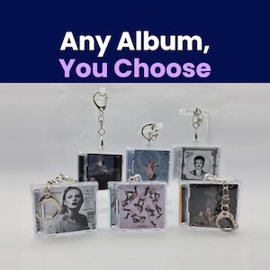 May include: A collection of six miniature square keychains featuring album cover art in clear plastic cases. Each keychain includes a silver-toned metal lobster clasp. The text "Any Album, You Choose" is displayed in white and light purple at the top.