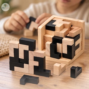 May include: A wooden block puzzle featuring a square frame and multiple L-shaped pieces in natural wood and black finishes. The set includes a partially assembled cube within the frame and several loose pieces arranged on a flat surface.