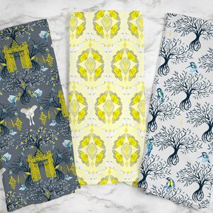 May include: Three decorative tea towels with unique patterns. One towel features a gray background with a tree design, birds, and a yellow arch. Another has a yellow butterfly pattern, and the third has a tree and bird design on a white background.