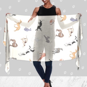 A woman wearing all black holding up a beige modal scarf with illustrated greyhound dog pattern on it.