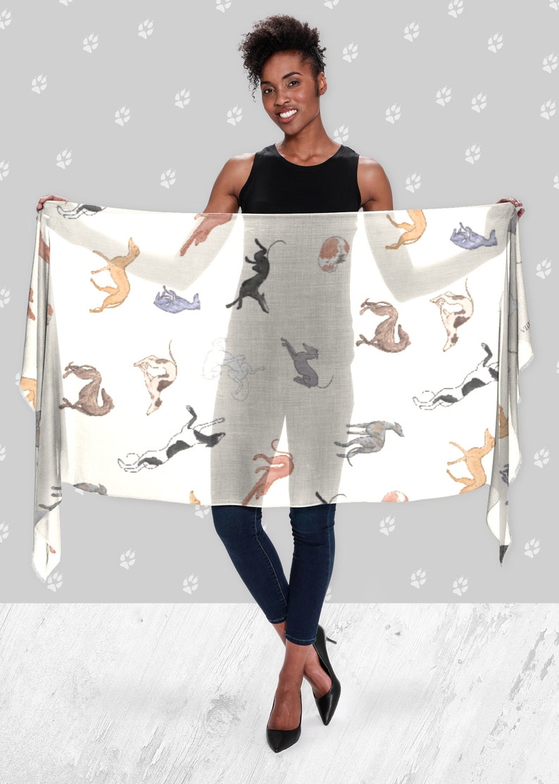A woman wearing all black holding up a beige modal scarf with illustrated greyhound dog pattern on it.