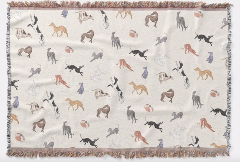 K&ouml;nnte beinhalten: Cremefarbene Decke mit einem sich wiederholenden Muster von Windhunden in verschiedenen Posen. Die Hunde sind in Schwarz-, Braun-, Grau- und Beiget&ouml;nen dargestellt. Die Decke hat einen Fransenrand.