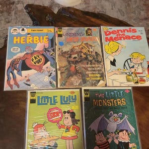 May include: A collection of five vintage comic books including Herbie, Grimm's Ghost Stories, Dennis the Menace, Little Lulu, and The Little Monsters. Each comic features colorful illustrated covers with character art and bold text titles.
