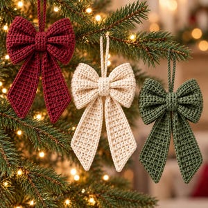May include: Three handmade crochet bow ornaments hanging from a pine tree. The set includes one deep red bow, one cream-colored bow, and one forest green bow. Each bow features a textured stitch pattern and a matching loop for hanging.