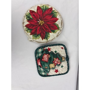 May include: A round quilted fabric potholder featuring a red poinsettia flower with green leaves on a cream background, paired with a square quilted potholder displaying a green Christmas tree graphic with red stars on a cream and green plaid base.