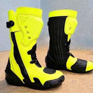 Puede incluir: Un par de botas de motocicleta de corte alto con un esquema de color amarillo neón vibrante y negro. Las botas incluyen espinilleras reforzadas, paneles negros texturizados, hebillas laterales ajustables y punteras protectoras con un acabado de goma duradero.